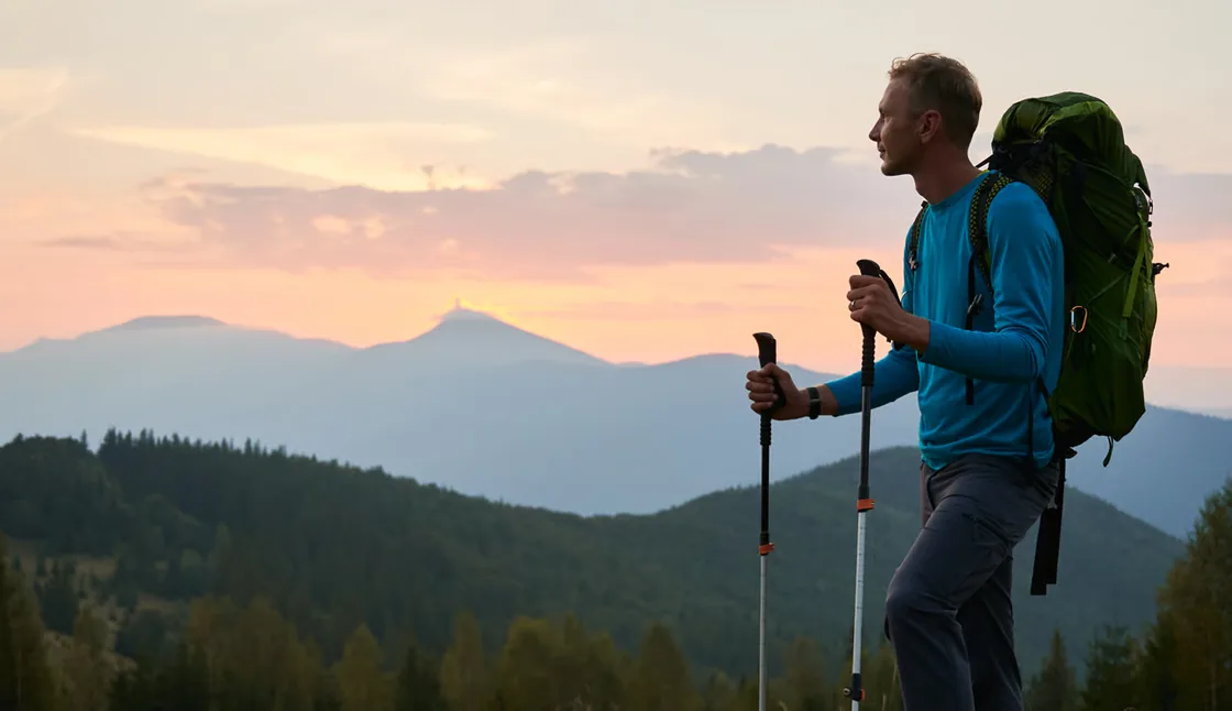 Hiker with a pack standing on a hilltop facing blue ridges at sunset