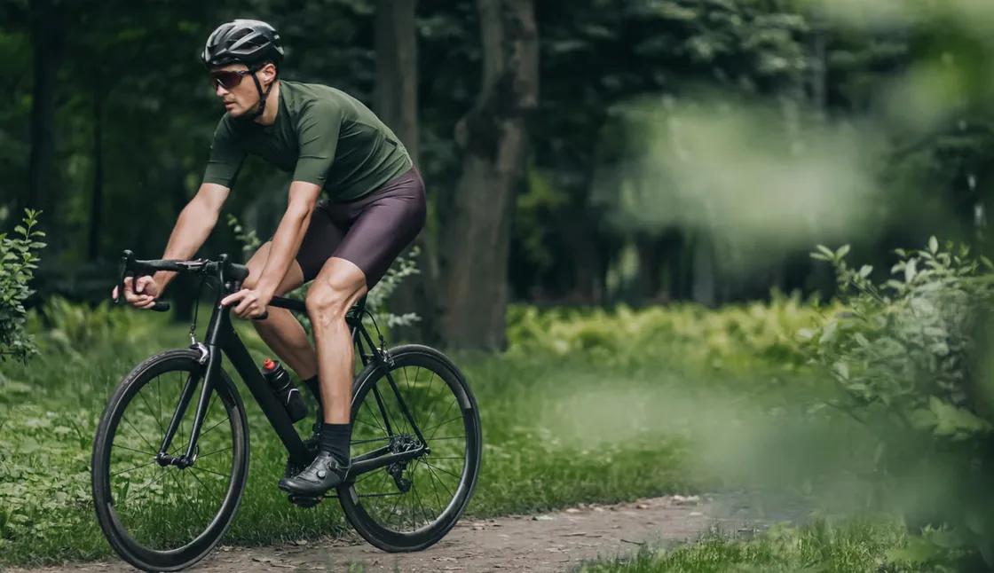 Cyclist in an olive green jersey riding fast along a forest track