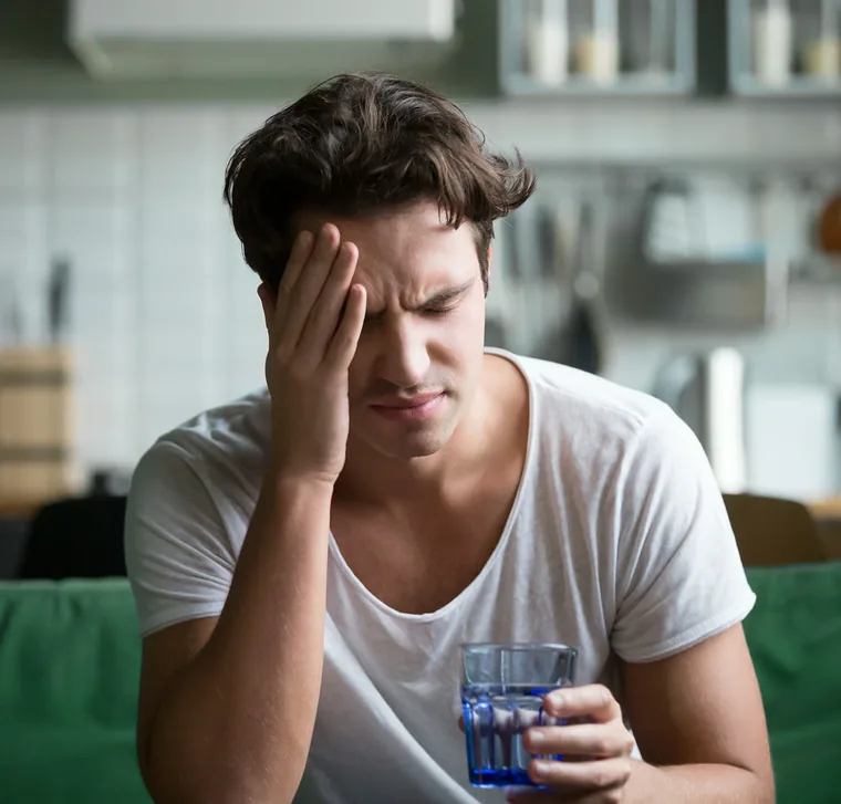 Tired man sitting in his kitchen with one hand pressed against his temple