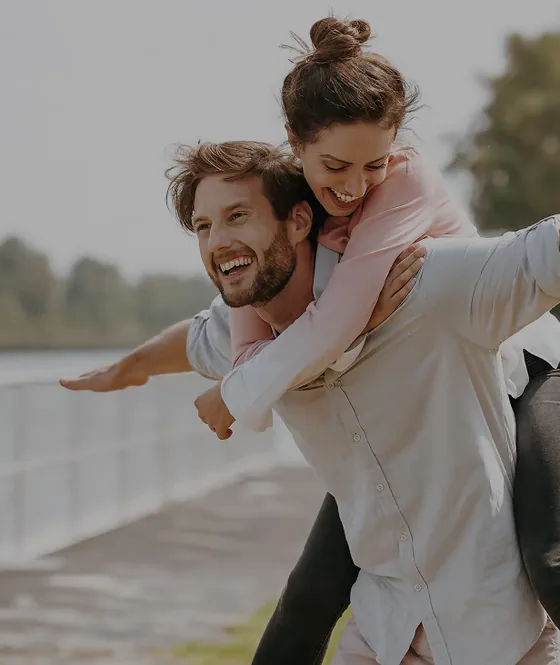 Man laughing while carrying a woman on his back along a lakeside path